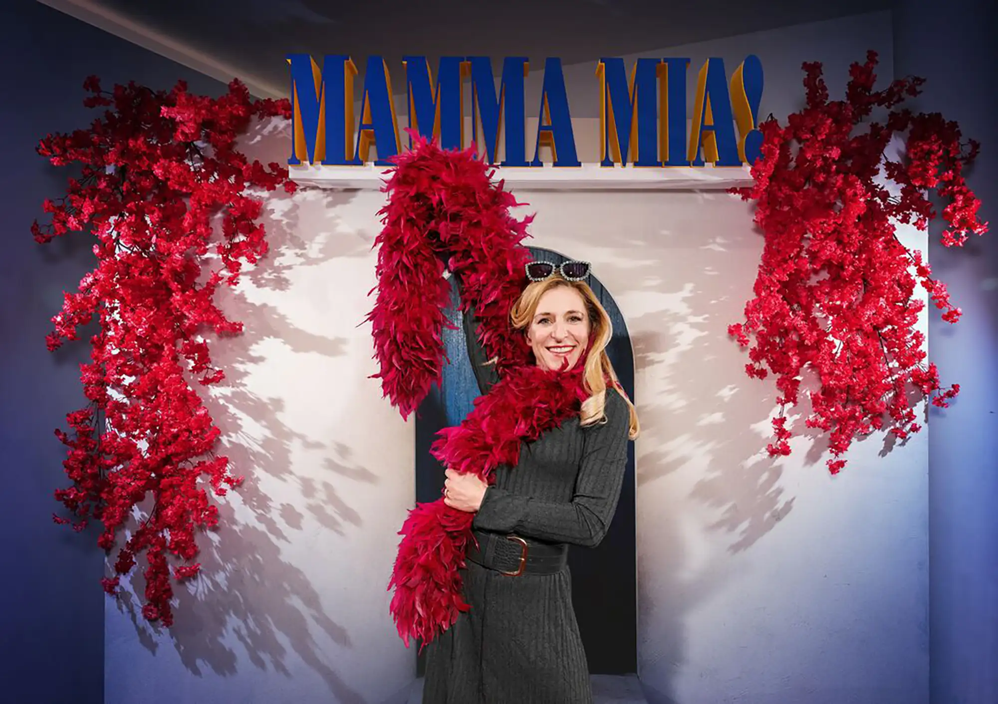 Stefanie Hertel mit einer roten Federboa vor dem Logo von Mamma Mia! in Hamburg